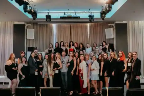 אלט טקסט: קבוצה של נשים וגברים באירוע יופי ומדיה, עומדים על במה עם תאורה מקצועית.