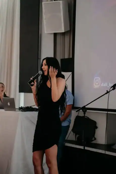 יפהפייה עם שיער כהה חורקי, מחייכת בזמן הופעה באירוע יופי ודוברות בדאלי בוטיק.